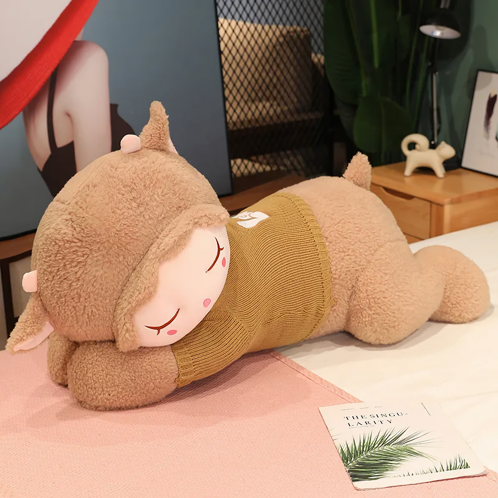 Dark brown sleeping sheep plush pillow with an olive knit sweater on a pink blanket