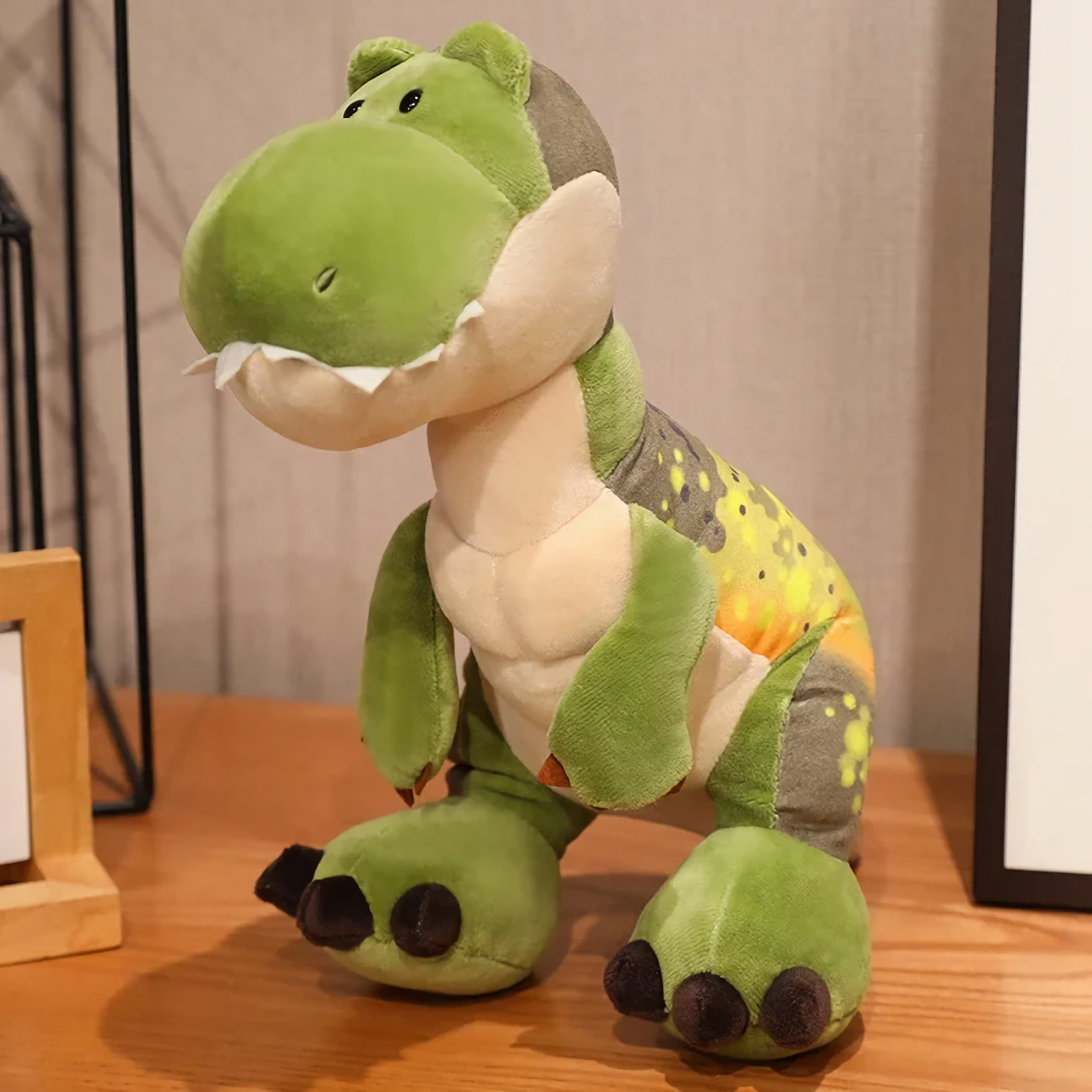 Green T-Rex dinosaur plush with a cream belly and dark feet sits on a wooden table.