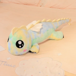 Rainbow green dragon plush with big eyes and cream wings on a pastel bed