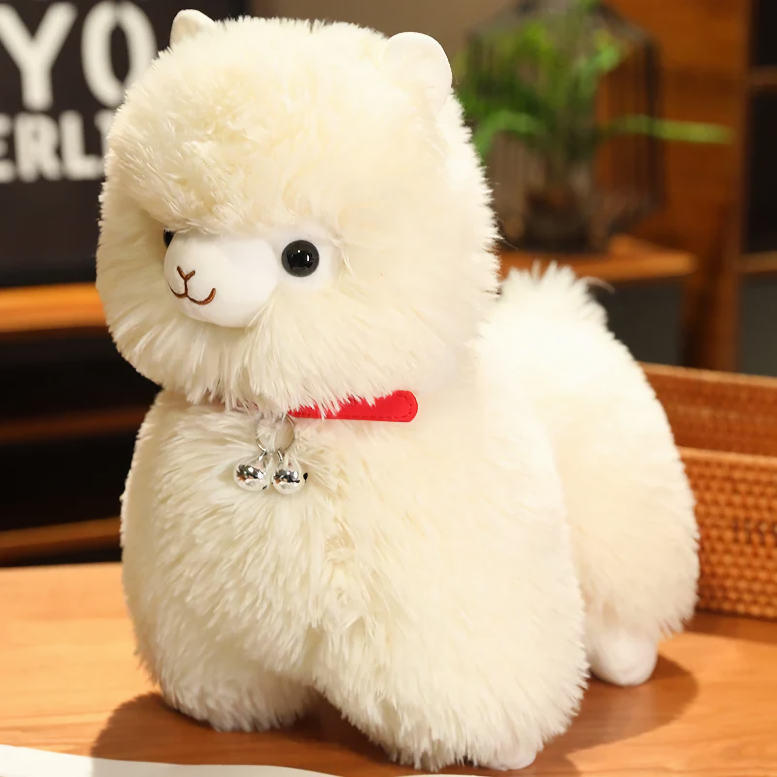 Close-up of a white alpaca plush with a red bell collar and black eyes