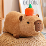 Lying capybara plush with an orange on its head on a woven stool