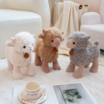 White, brown and gray curly lamb plushies on a white rug beside a cup and magazine