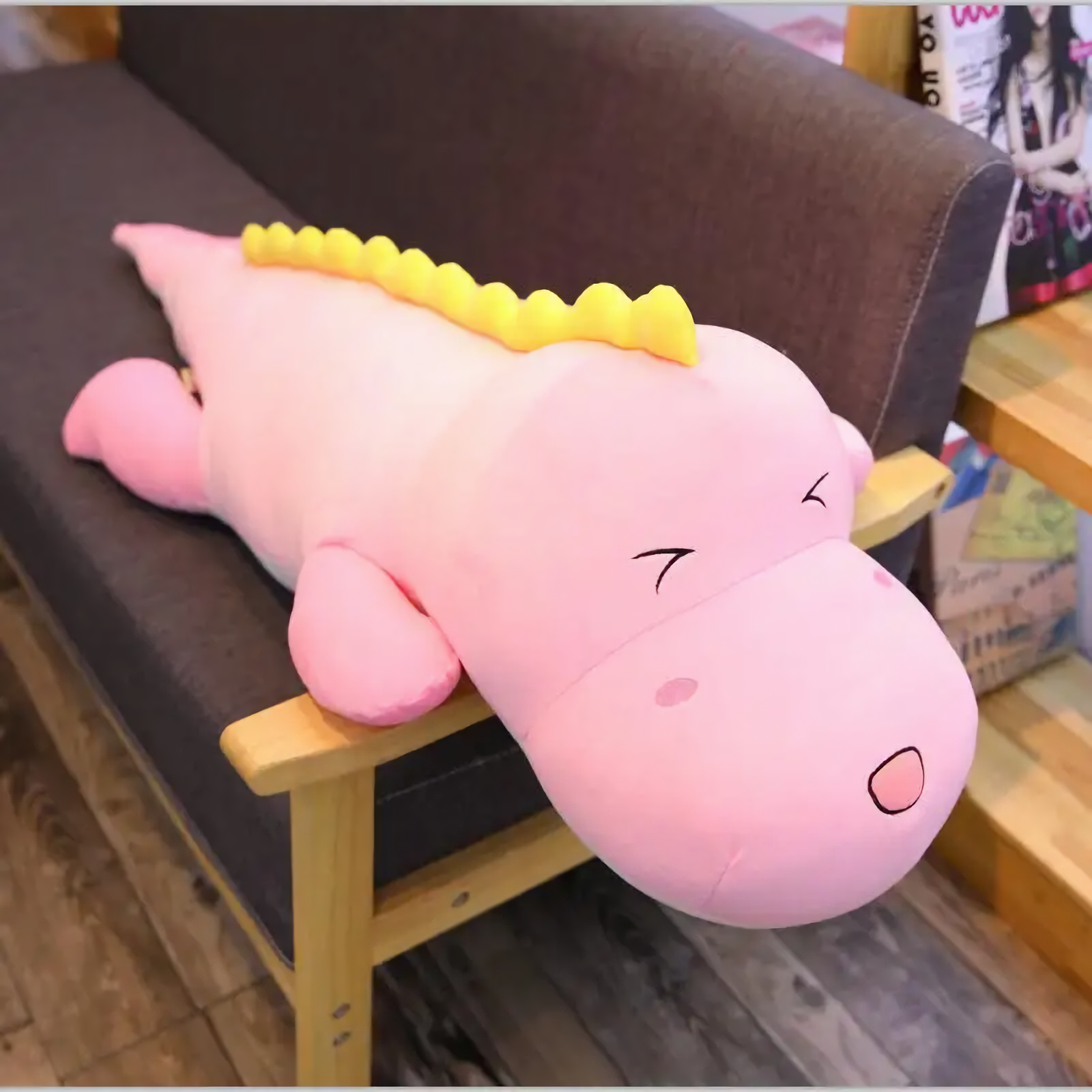 Pink dinosaur plush body pillow with a yellow ridge lying on a sofa