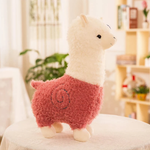 Pink body alpaca plush with a white head and a stitched swirl on a table
