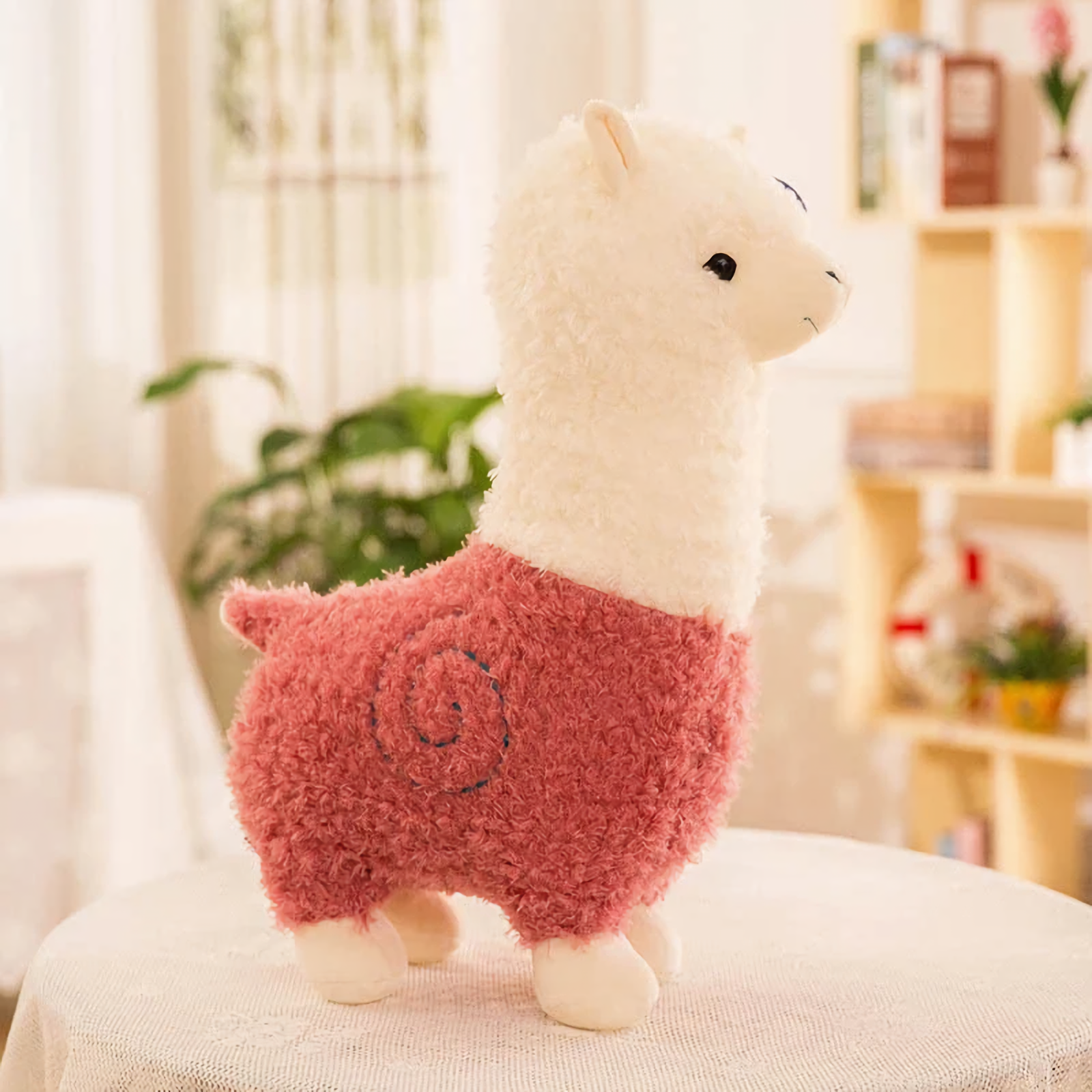 Pink body alpaca plush with a white head and a stitched swirl on a table