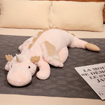 Pink and white dragon plush body pillow on a bed with cream pillows.
