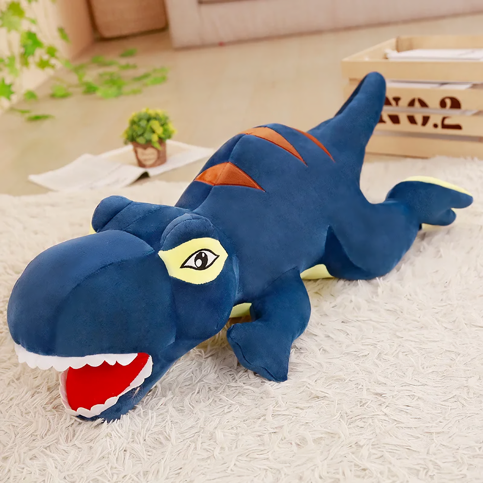Long blue T-Rex plush pillow with orange stripes and yellow eyes lying on a rug