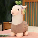 Gray alpaca plush with rainbow headphones and a leaf sprout on a bed