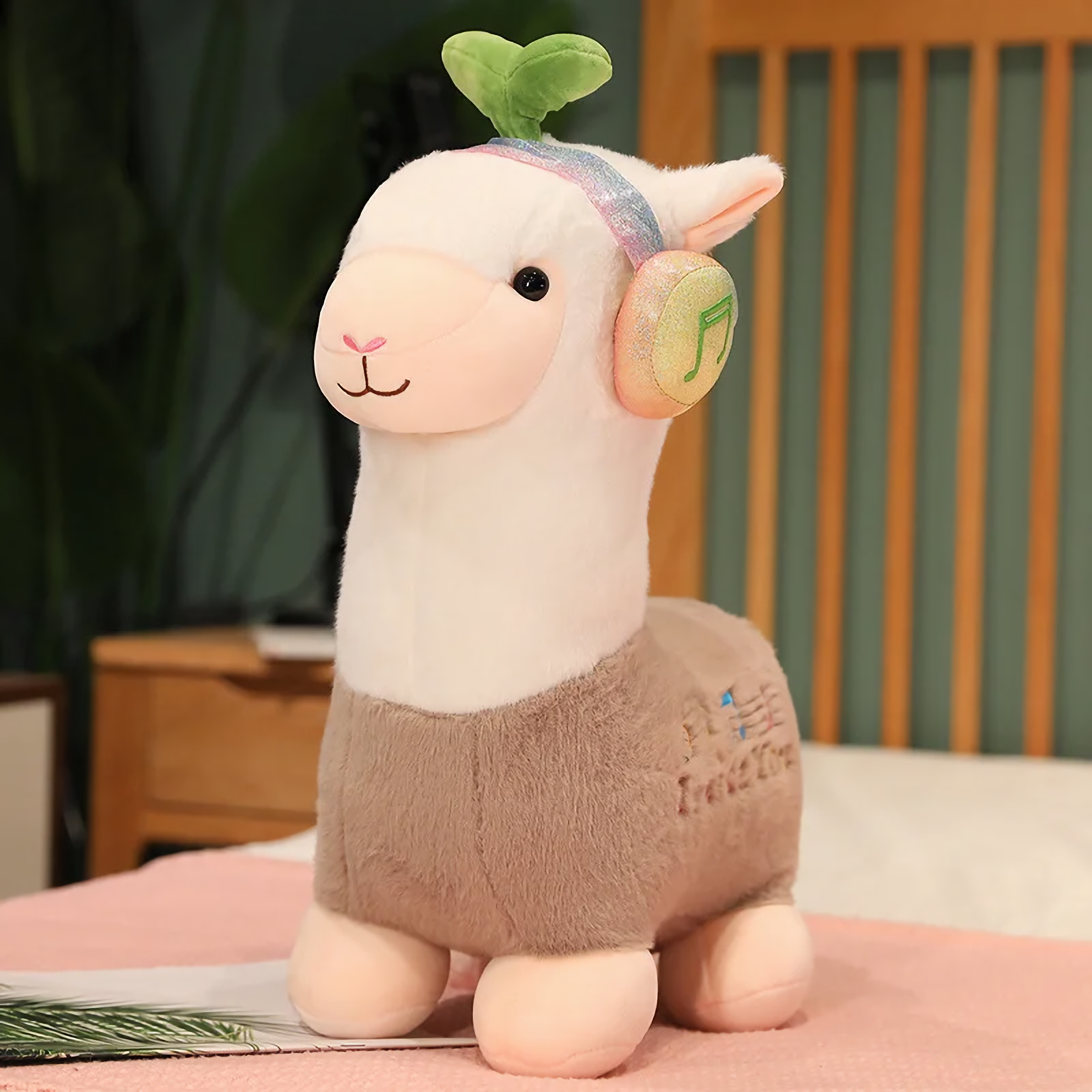 Gray alpaca plush with rainbow headphones and a leaf sprout on a bed