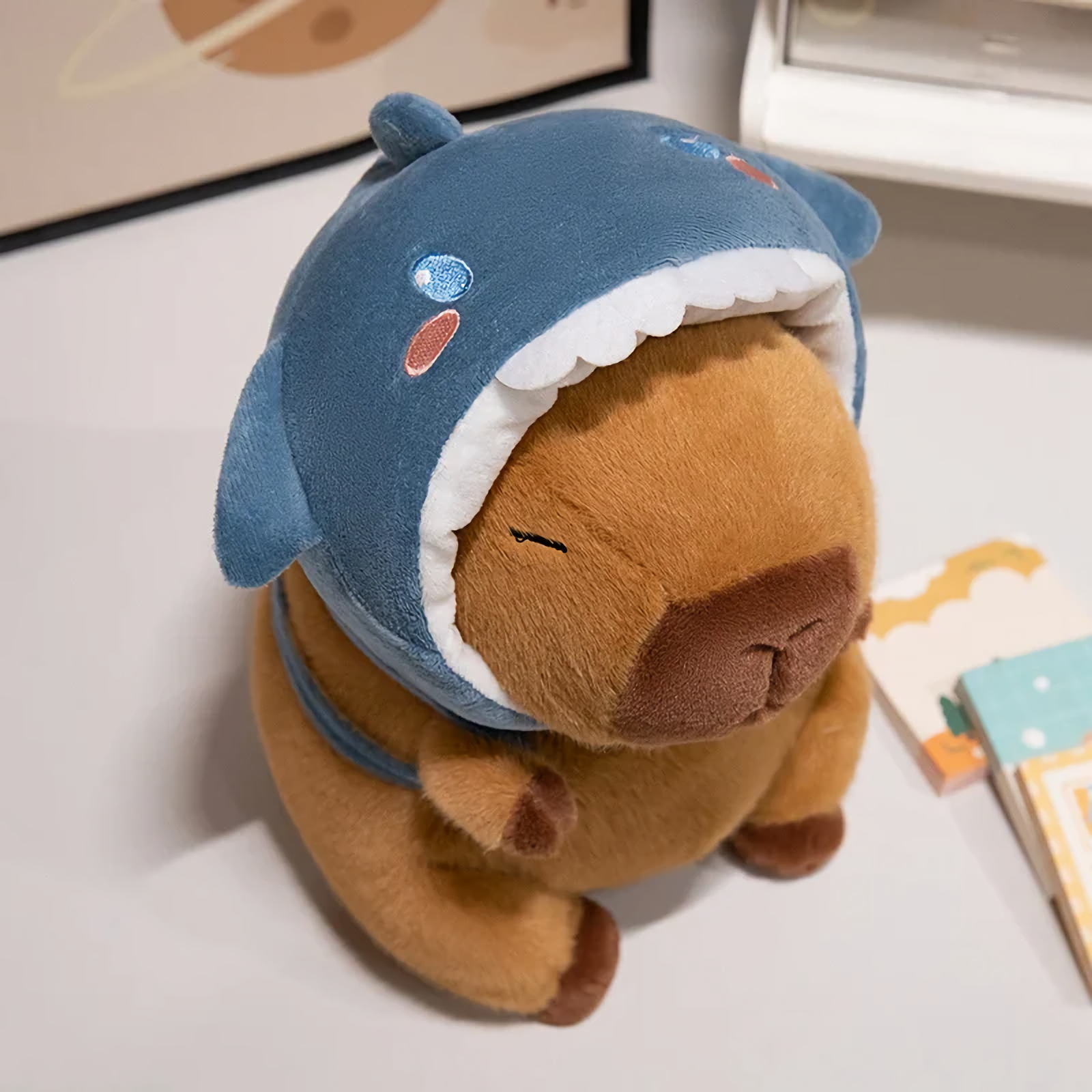 Capybara plush in a blue shark hood on a white table