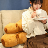 Woman drinking tea beside two lying capybara plush pillows on a sofa