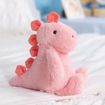 Pink dinosaur plush sitting on a white bed