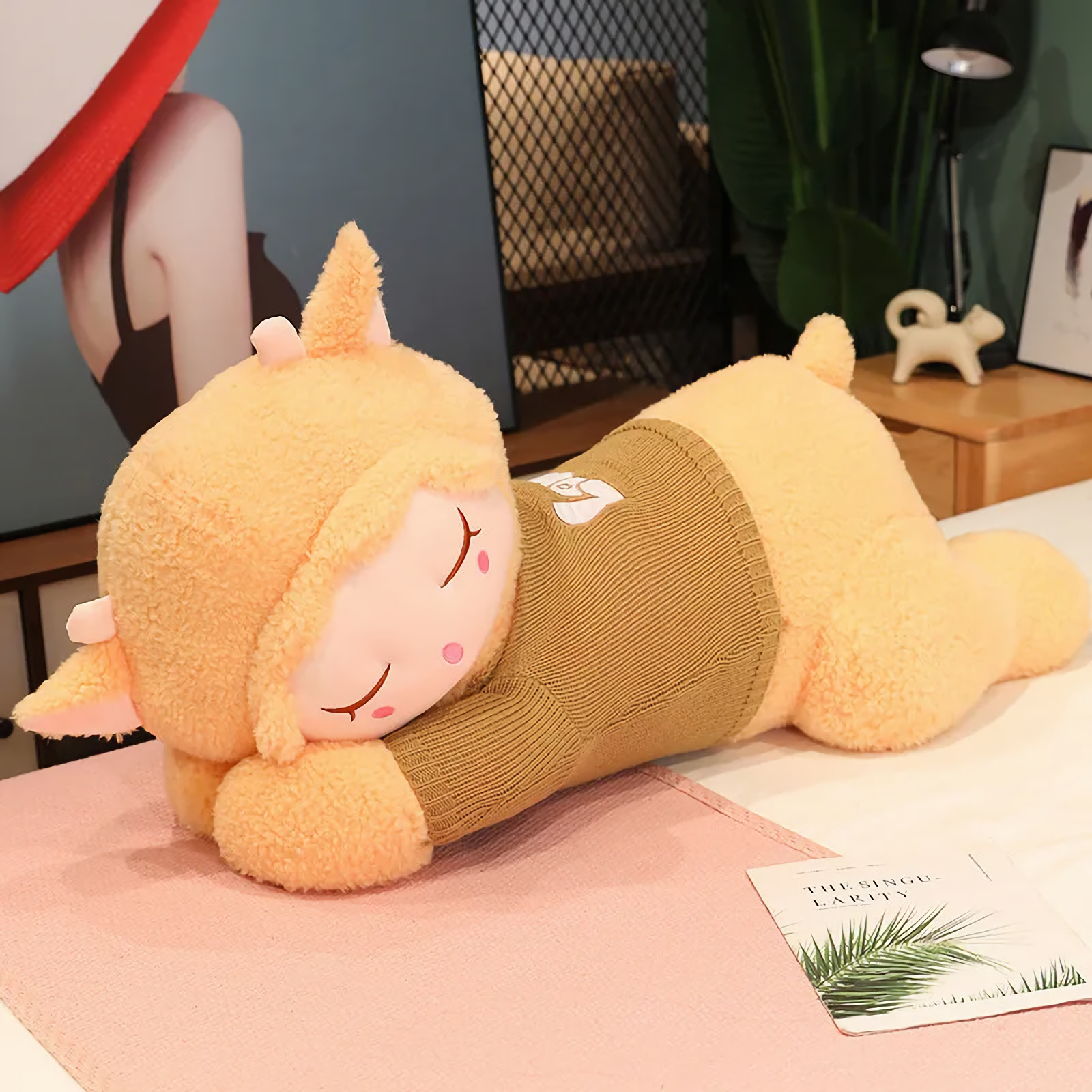 Light brown sleeping sheep plush pillow with an olive knit sweater on a pink blanket
