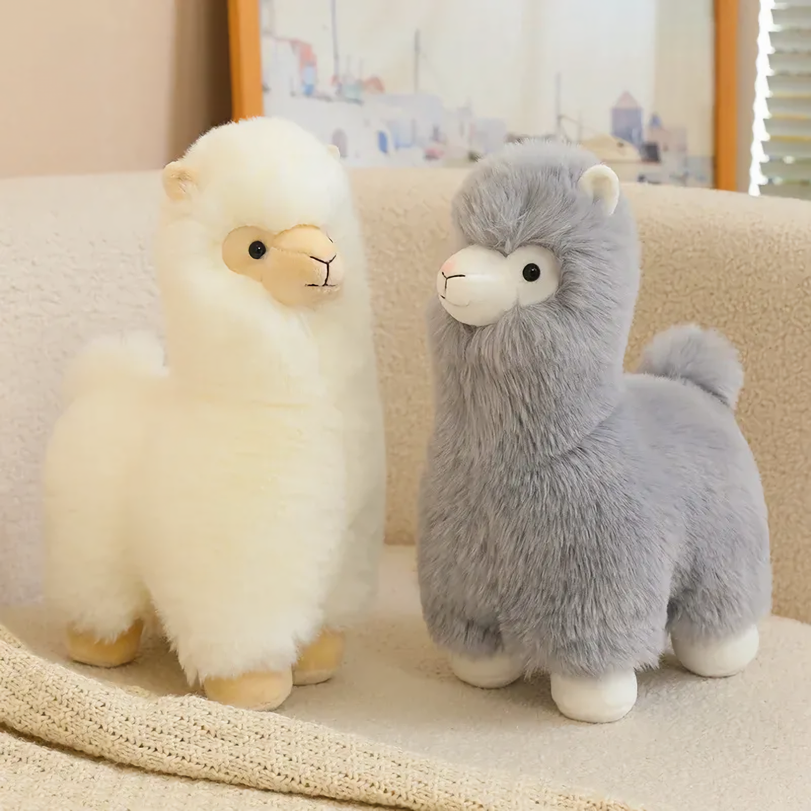 White and gray alpaca plushies sitting together on a cream sofa