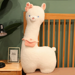 White alpaca plush with a pink bow and a pink mini bag standing on a bed