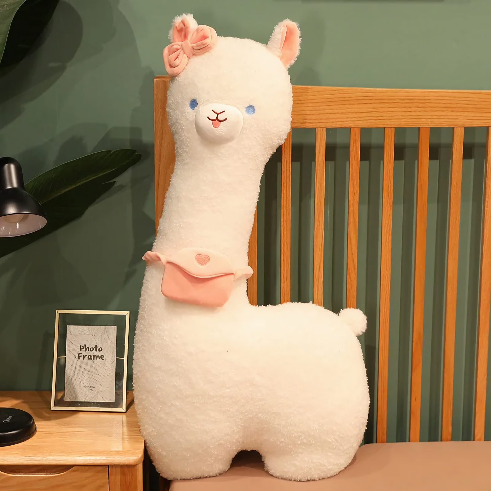 White alpaca plush with a pink bow and a pink mini bag standing on a bed