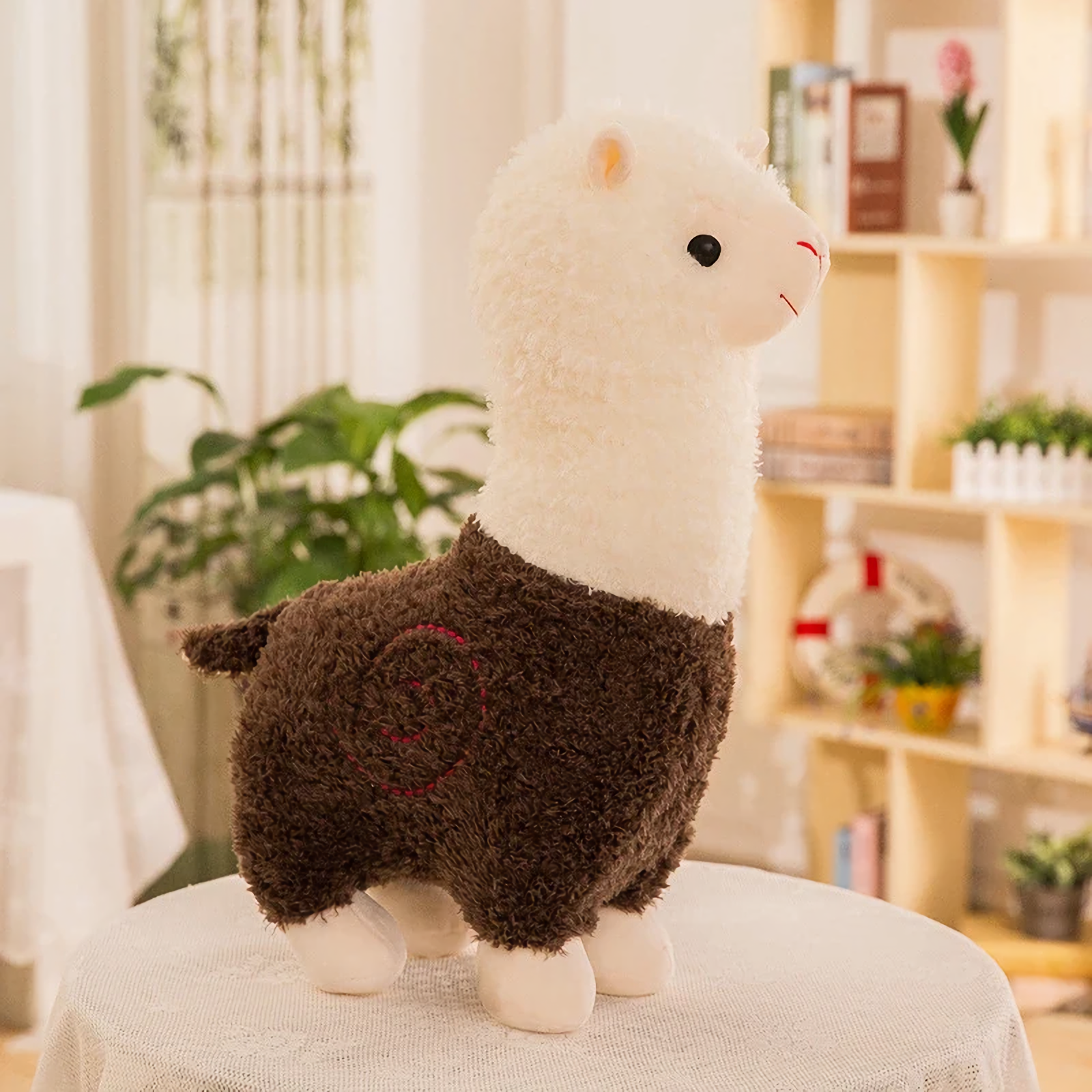 Brown body alpaca plush with a white head and a stitched swirl on a table