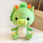 Green dragon plush with orange horns sitting on a white sofa.