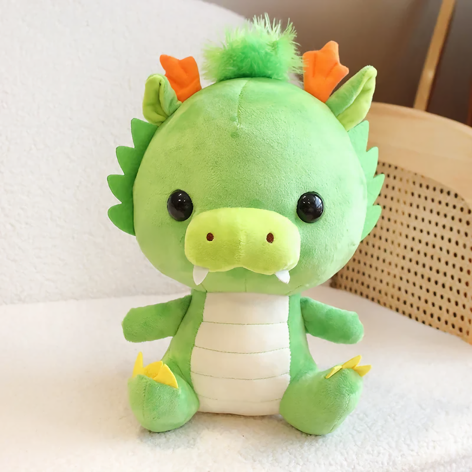 Green dragon plush with orange horns sitting on a white sofa.