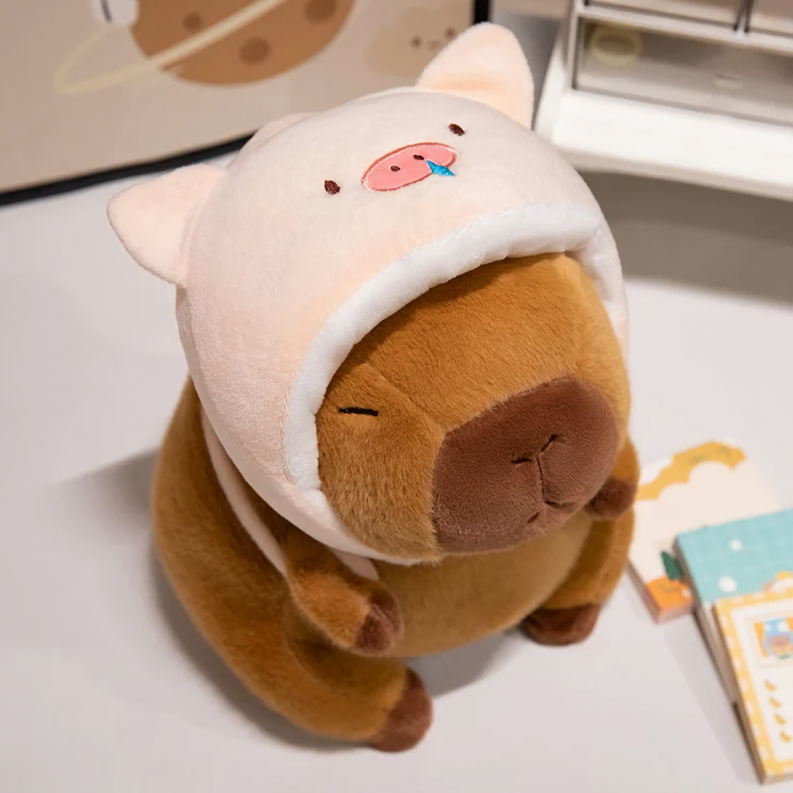 Capybara plush in a pink pig hood on a white table