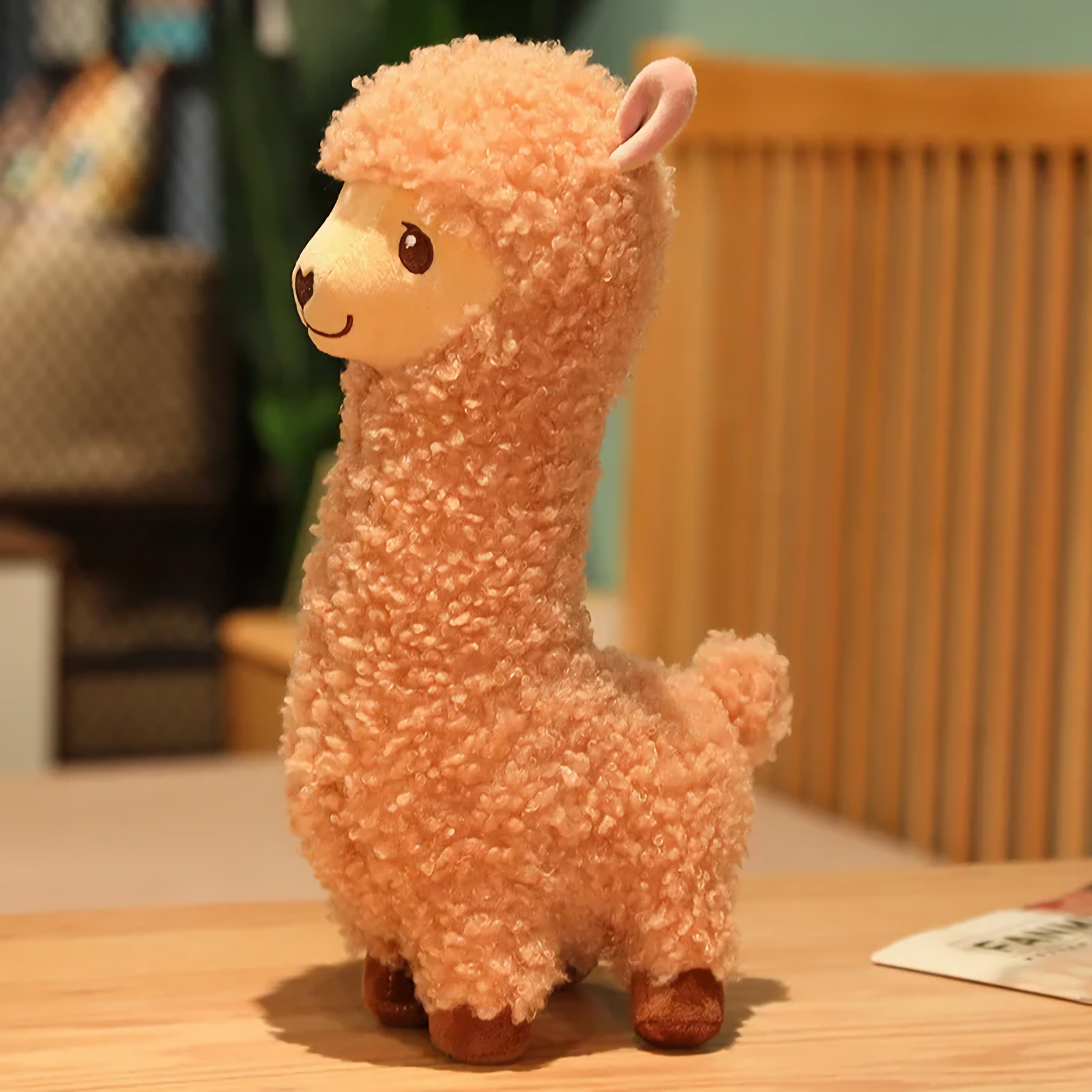 Brown alpaca plush with a long neck and cream face standing on a bed