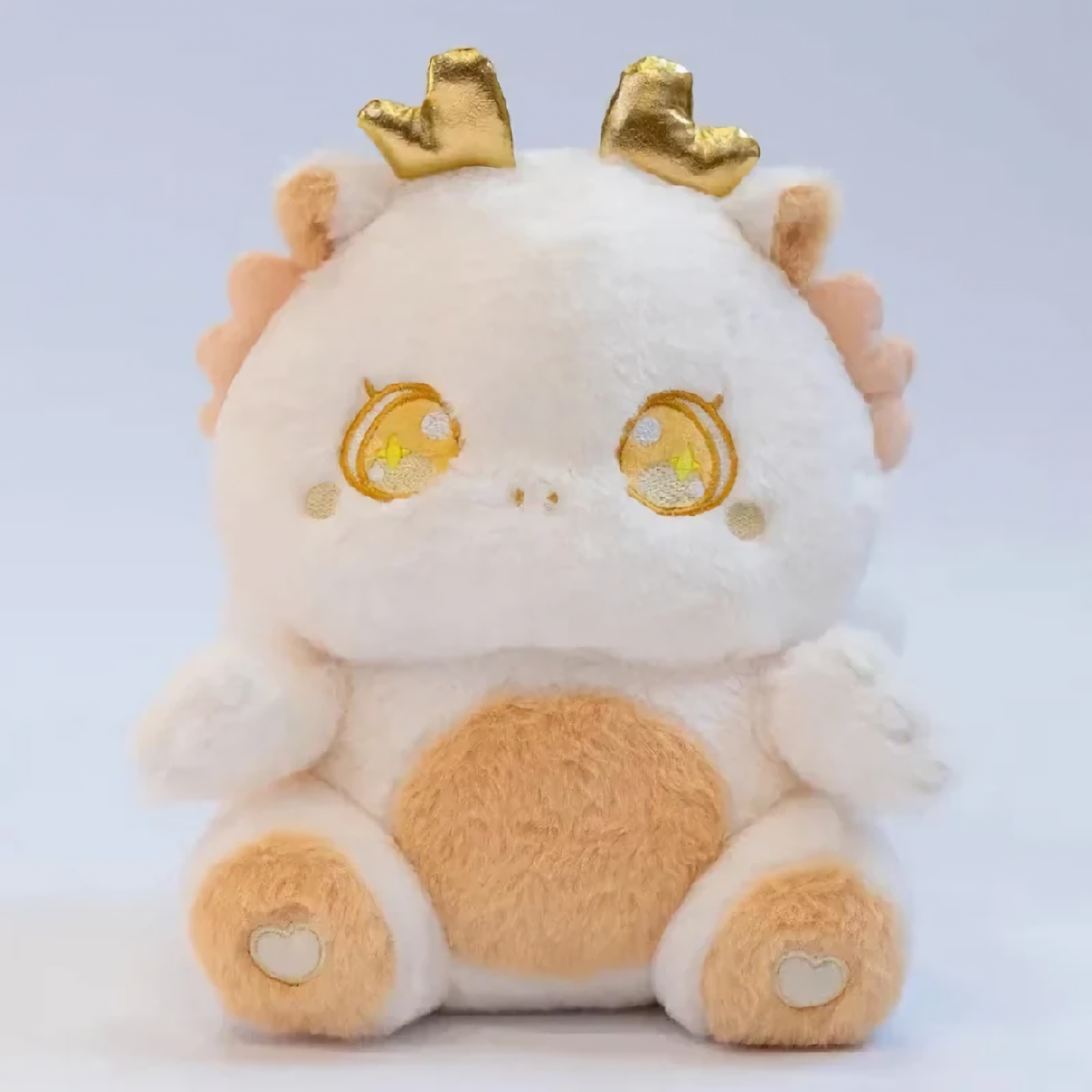 White fluffy baby dragon plush with golden horns and sparkly star eyes, close-up of face on light background.