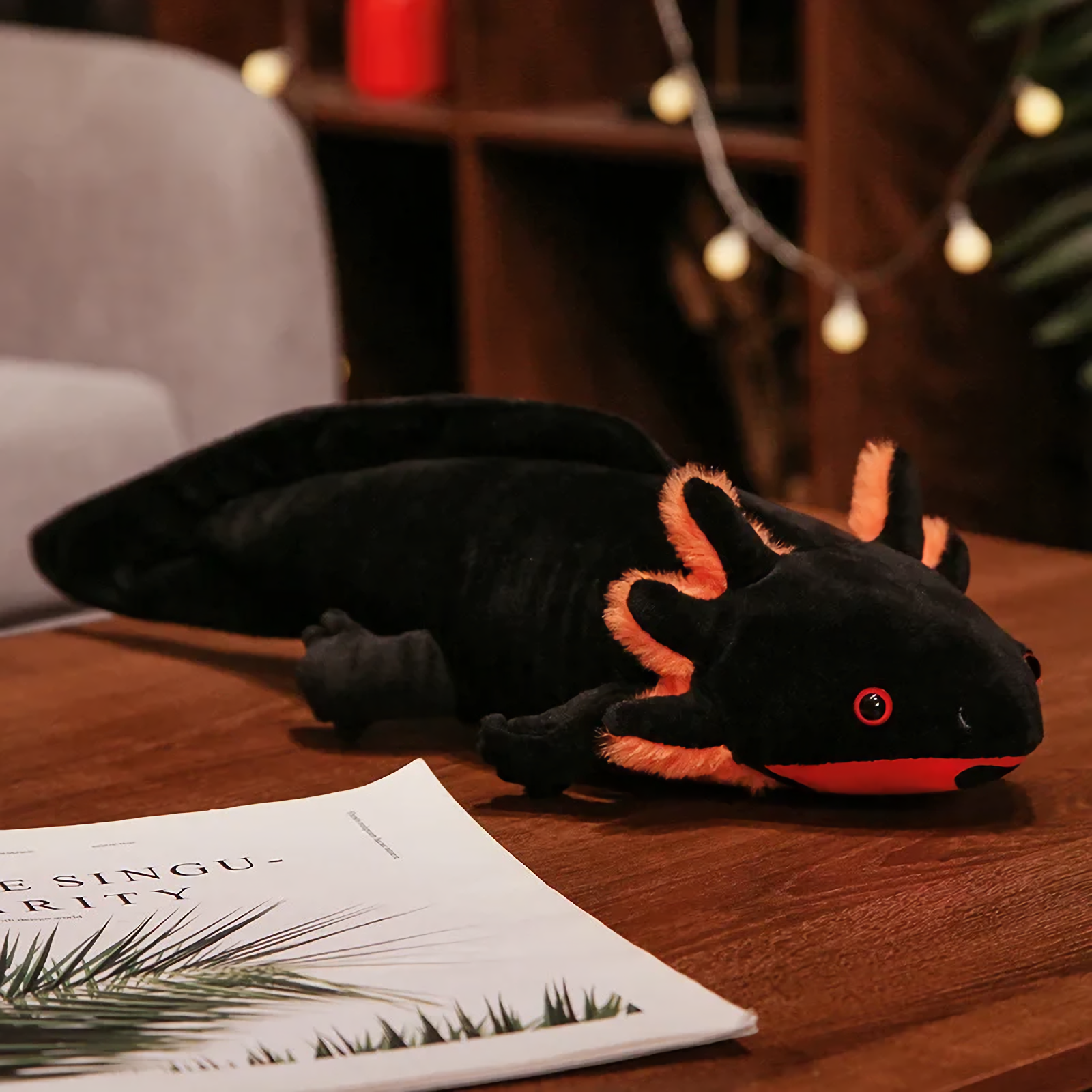 Black axolotl plush with orange gills and a red mouth on a wooden table