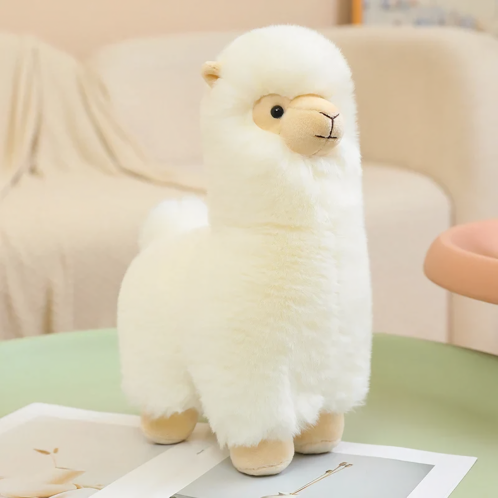 White alpaca plush with a cream face and tan nose on a green table