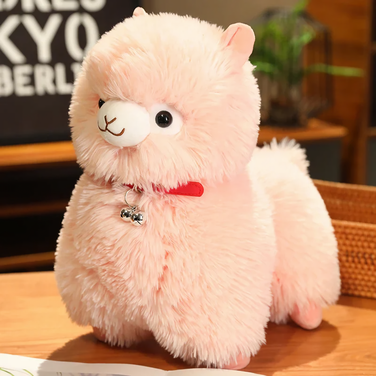 Pink alpaca plush with a red bell collar and a fluffy tail