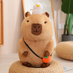 Sitting capybara plush with a white duck and an orange charm on a woven stool
