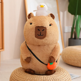 Sitting capybara plush with a white duck and an orange charm on a woven stool