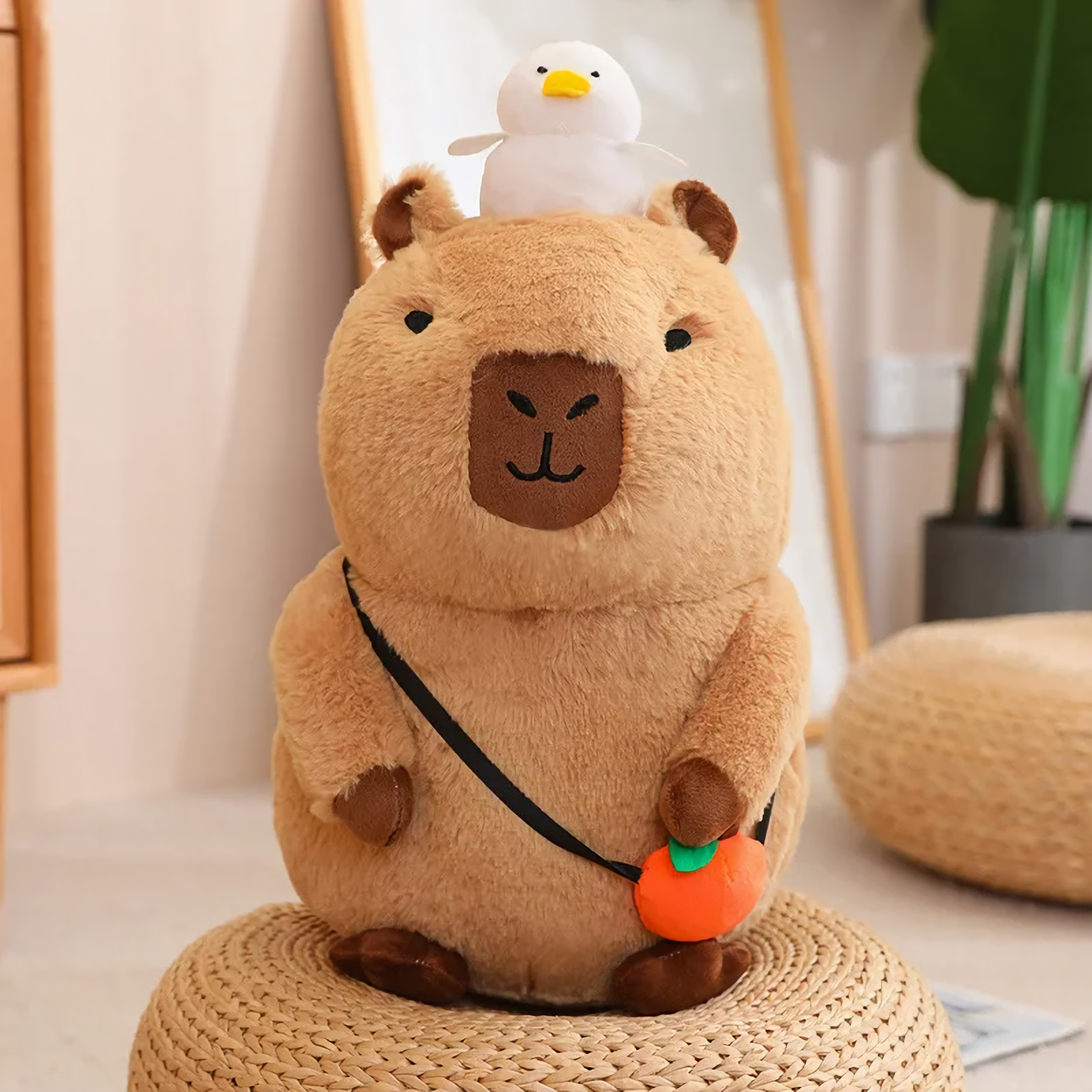 Sitting capybara plush with a white duck and an orange charm on a woven stool