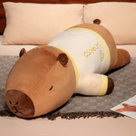 Lying capybara plush pillow in a cream shirt with yellow trim on a bed