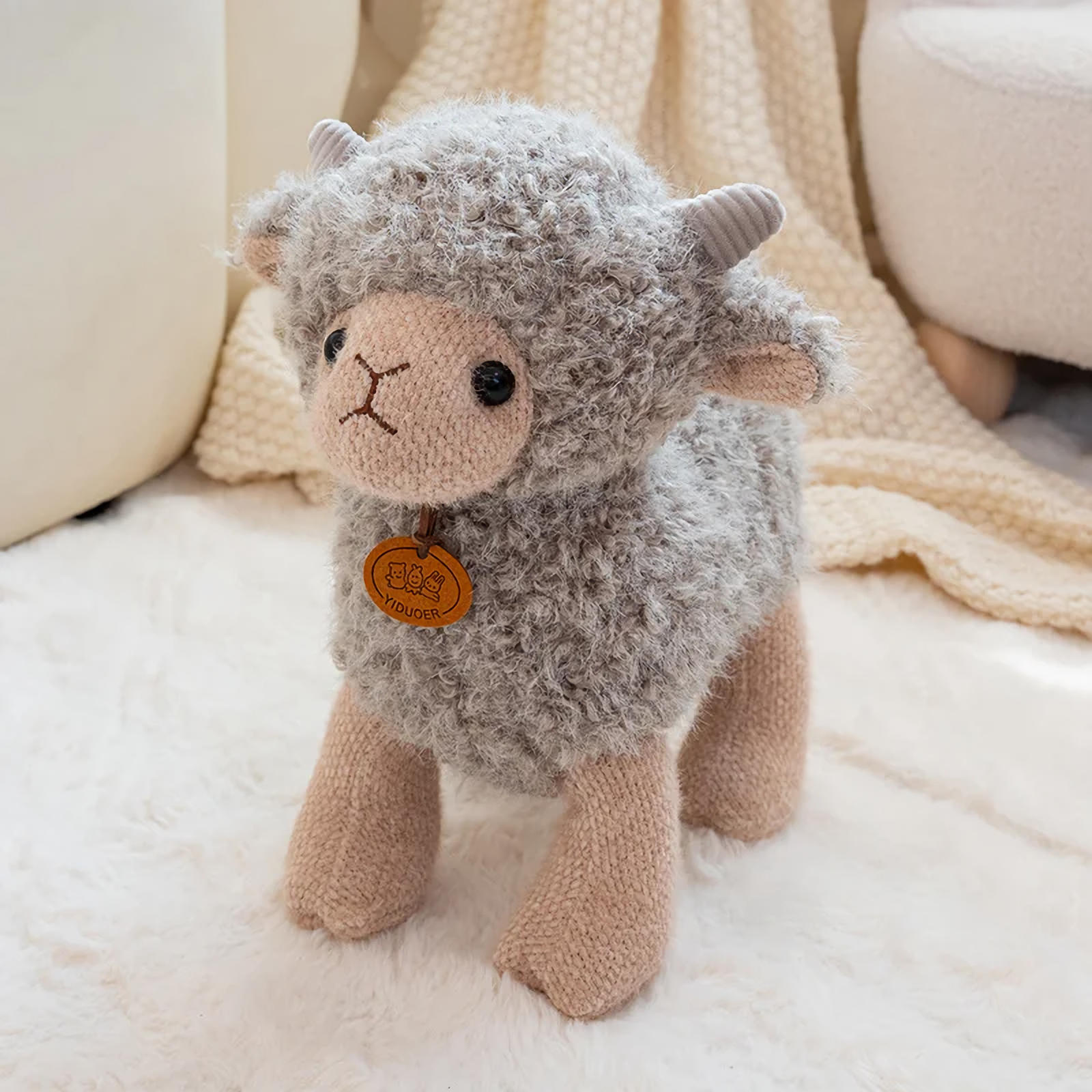 Gray curly lamb plush with tiny horns and an orange chest tag