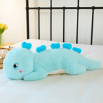 Blue giant dinosaur plush body pillow on a bed, showing heart-shaped back spikes and star cheek mark.