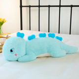 Blue giant dinosaur plush body pillow on a bed, showing heart-shaped back spikes and star cheek mark.