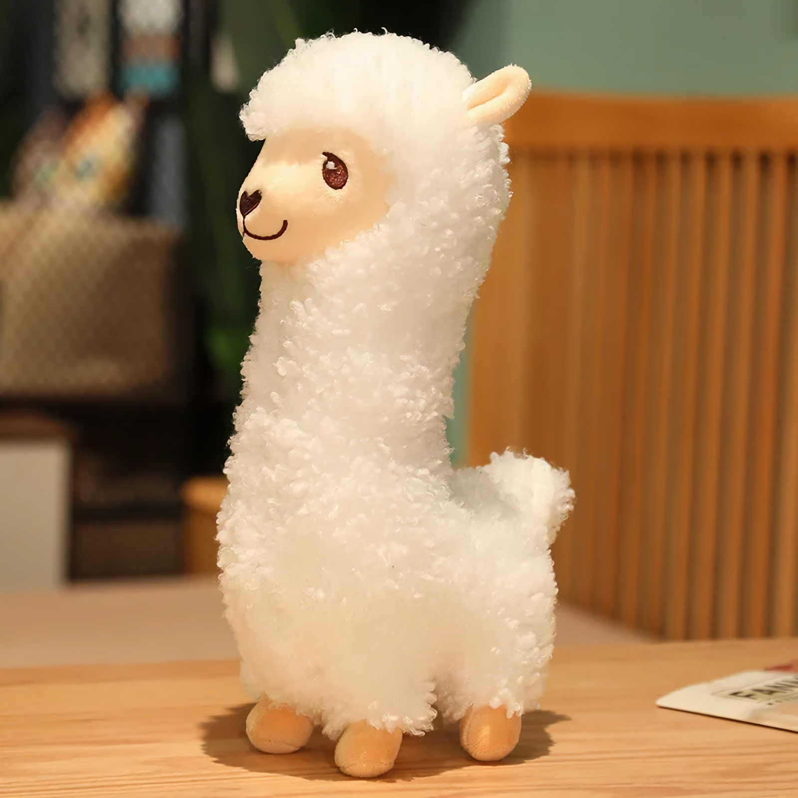 White alpaca plush with a long neck and cream face standing on a bed
