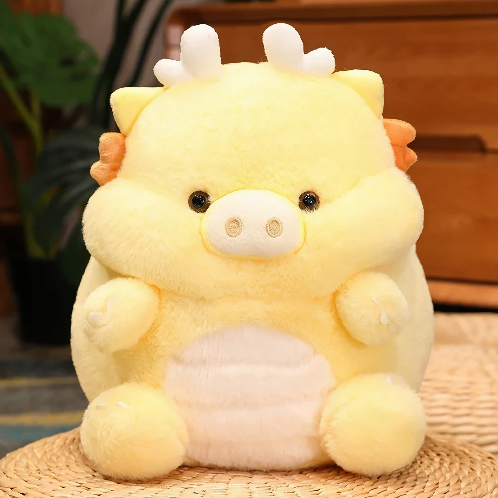 Yellow kawaii pig-dragon plush with tiny horns and cream belly on woven mat, close-up of face.