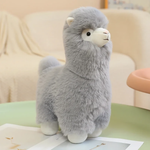 Gray alpaca plush with a cream face and tan nose on a green table