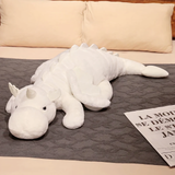 White dragon plush with a small horn and soft wings lying on a gray bed