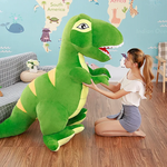 A person kneels beside a large green dinosaur plush toy in a colorful room with a world map on the wall.