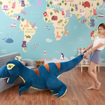 A person pulls a large blue dinosaur plush toy in a room with a world map mural on the wall.