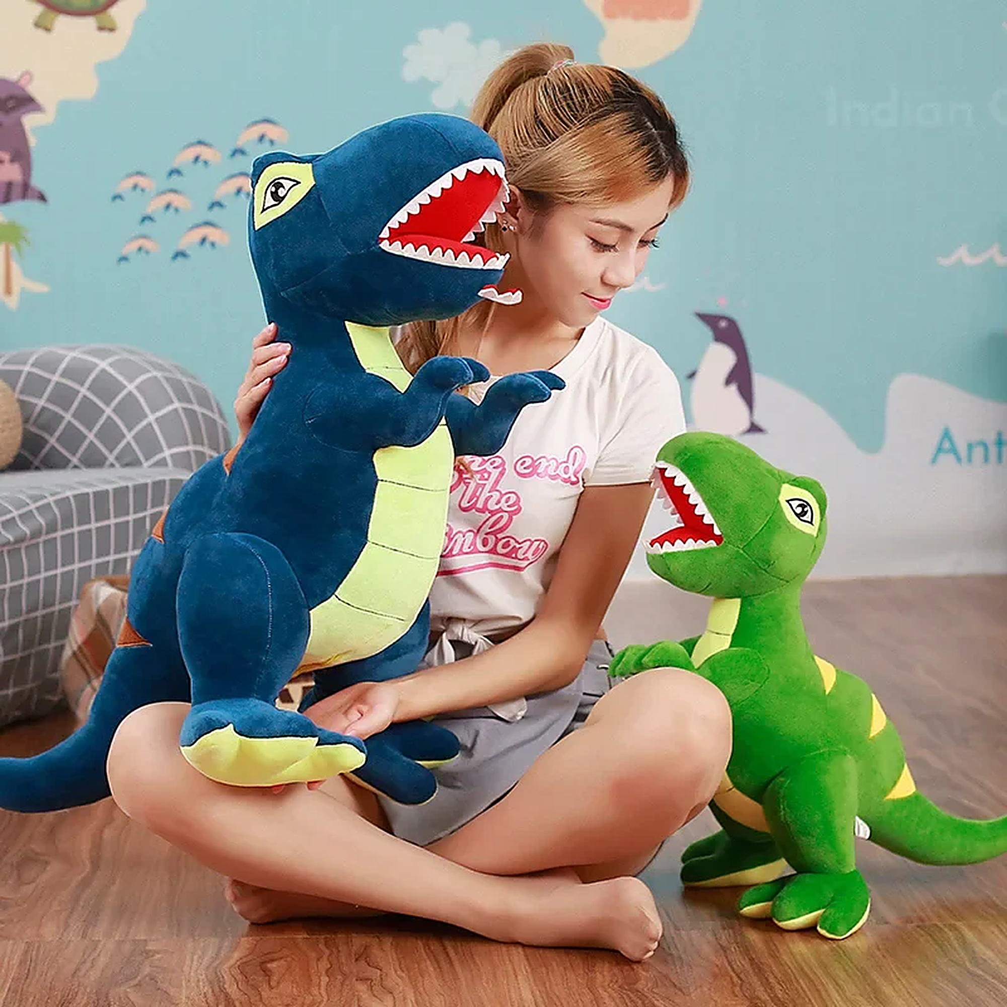 A person sits on the floor with two plush dinosaur toys, one blue and one green, in a colorful room.