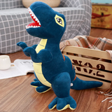 Plush T-Rex dinosaur toy with blue and yellow colors, sitting on a wooden floor beside a crate and a blanket.