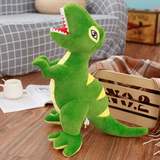 Green plush T-Rex toy with yellow accents, standing on a wooden floor near a basket and a cup.
