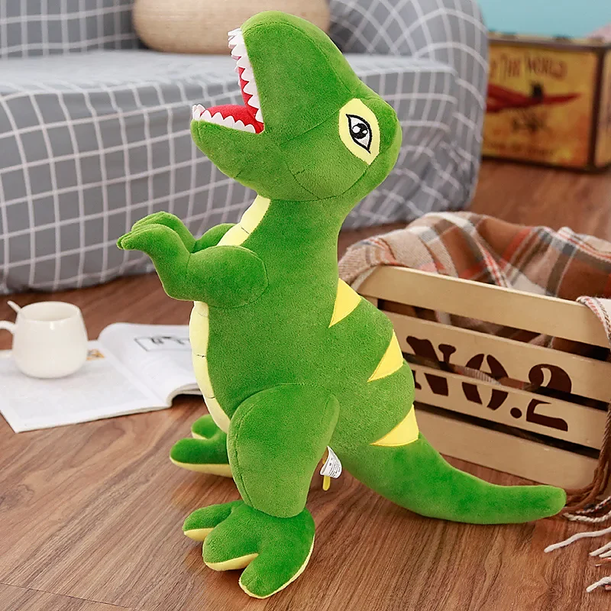 Green plush T-Rex toy with yellow accents, standing on a wooden floor near a basket and a cup.