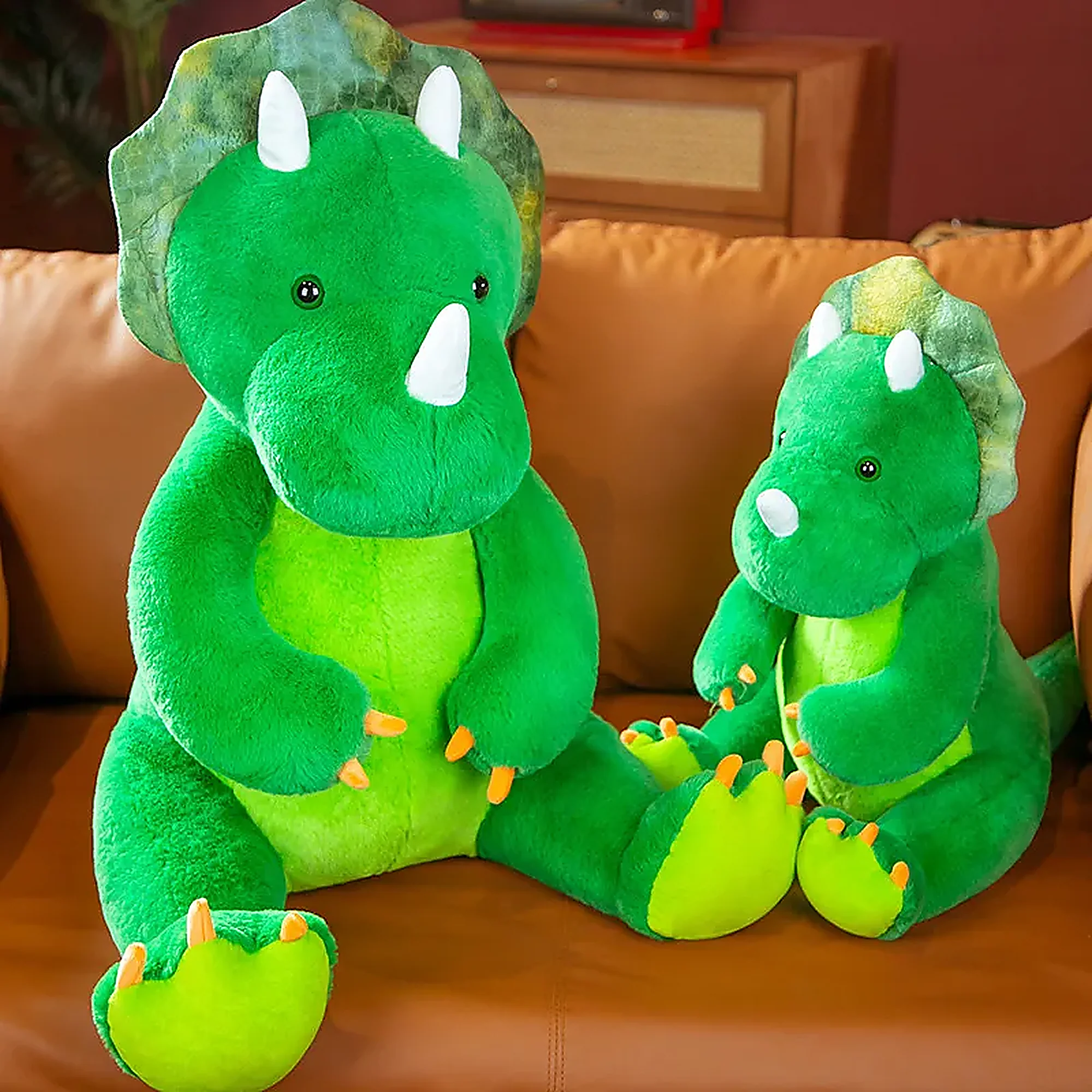 Two green triceratops plush toys, one large and one small, sitting on a brown couch.