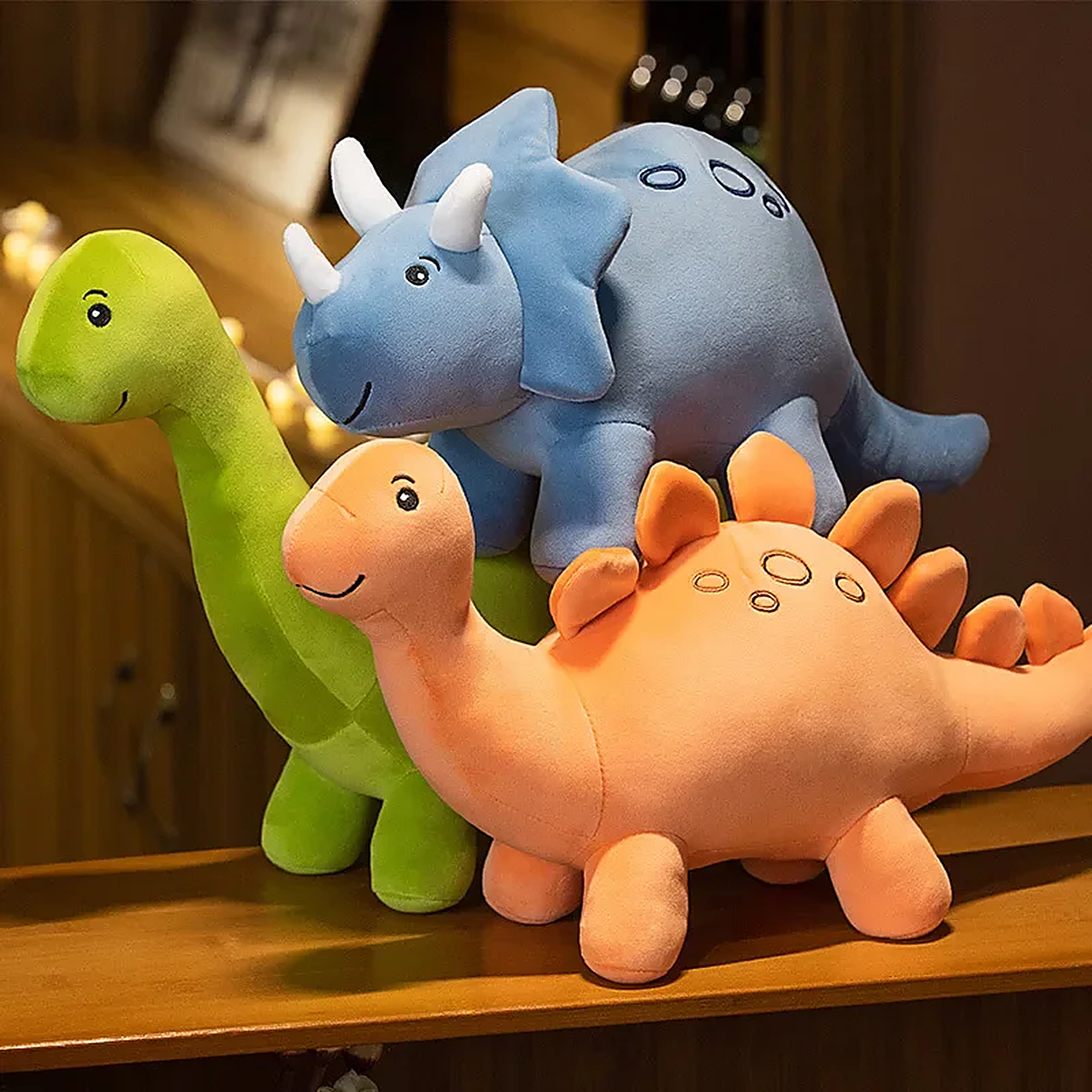 Colorful plush dinosaur toys in green, blue, and orange stacked on a wooden surface.