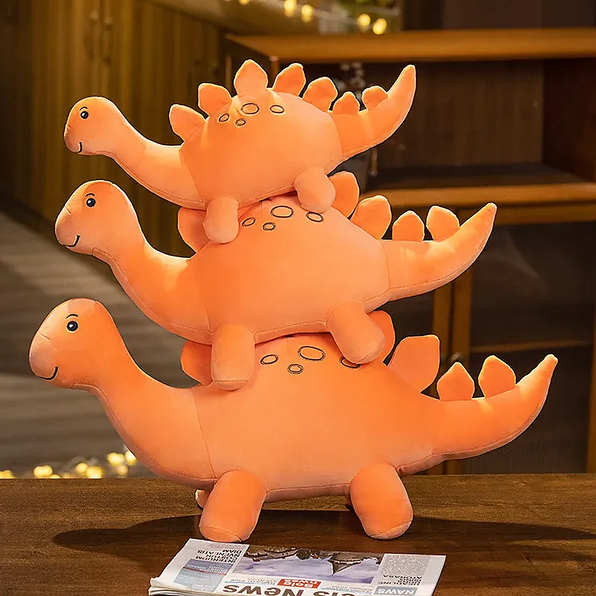 Three stacked orange dinosaur plush toys with smiling faces and spiky backs, sitting on a table.