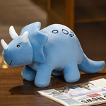 Blue plush triceratops toy with white horns and a smiling face, sitting on a table next to a newspaper.